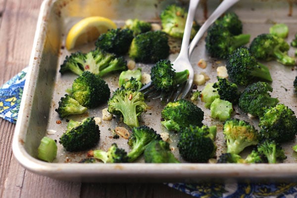 Roasted broccoli on a baking pan with lemon wedges and two forks.