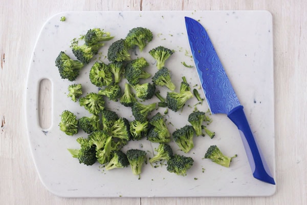 Raw broccoli florets on a cutting board with a blue knife.