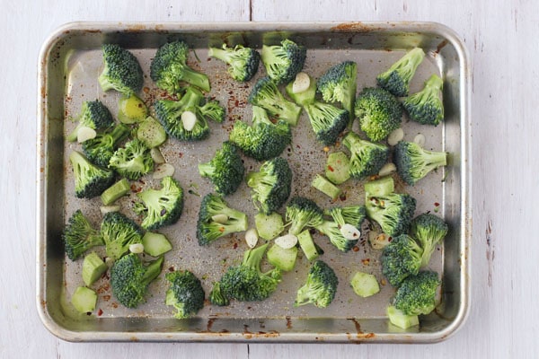 Raw broccoli on a quarter sheet pan with garlic slices.