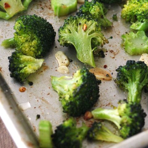 Toaster oven roasted broccoli on a baking pan with red pepper flakes and garlic slices.