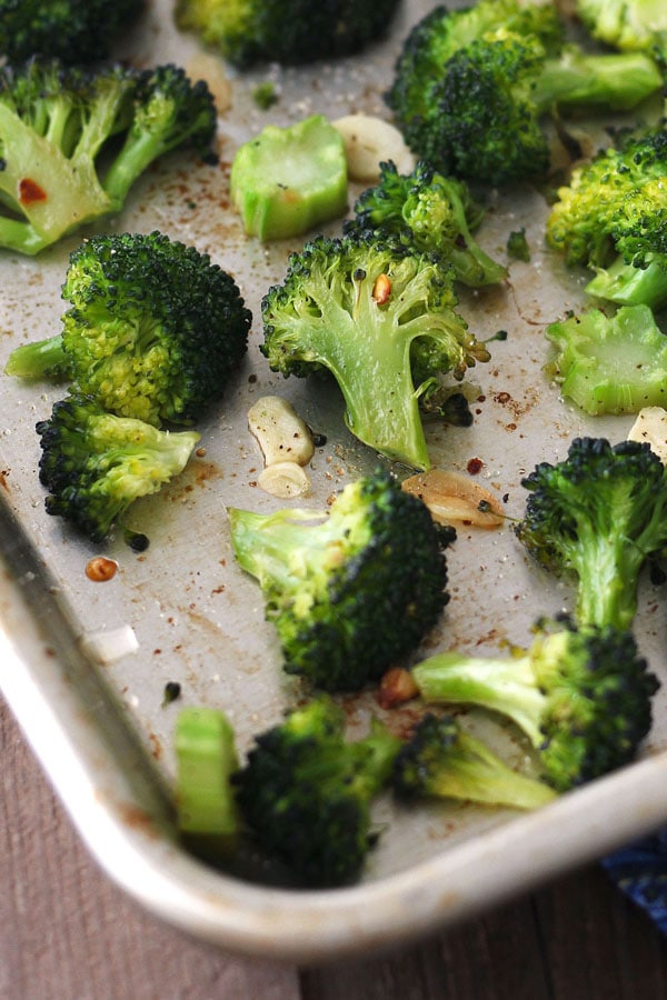 Toaster oven roasted broccoli on a baking pan with red pepper flakes and garlic slices.