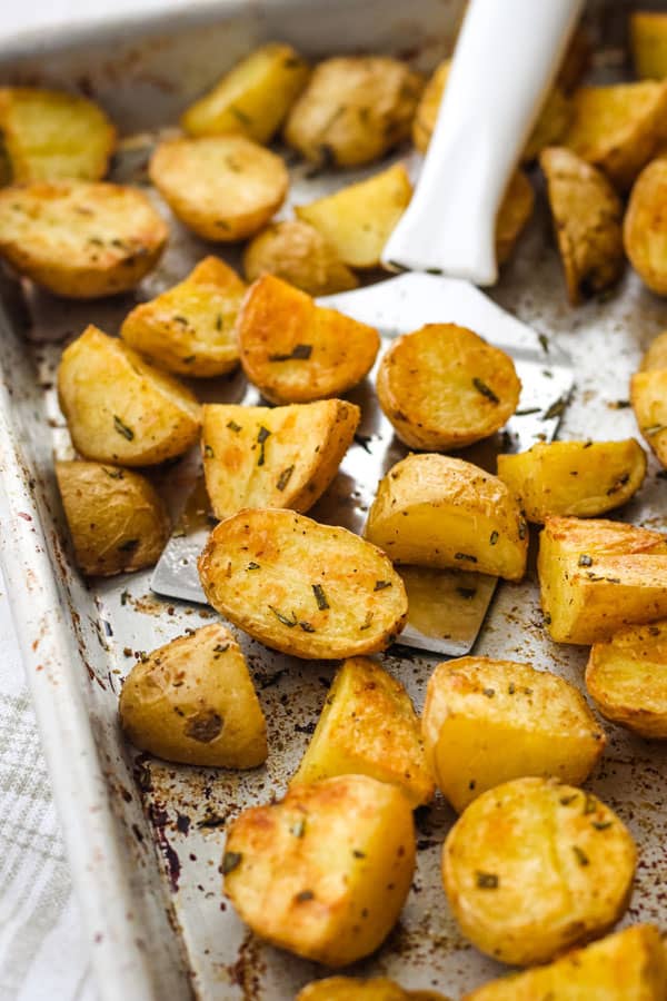 Roasted potatoes on a metal baking pan with a spatula.