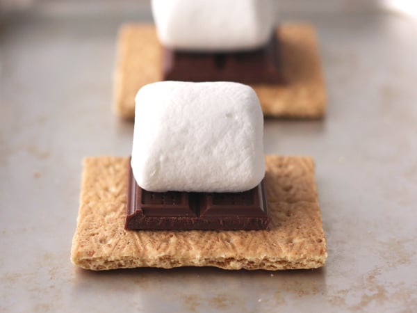 Graham crackers topped with chocolate and marshmallows on a toaster oven pan.