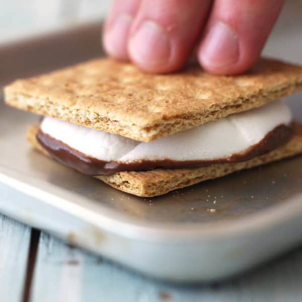 Fingers pressing a graham cracker into a s'more.