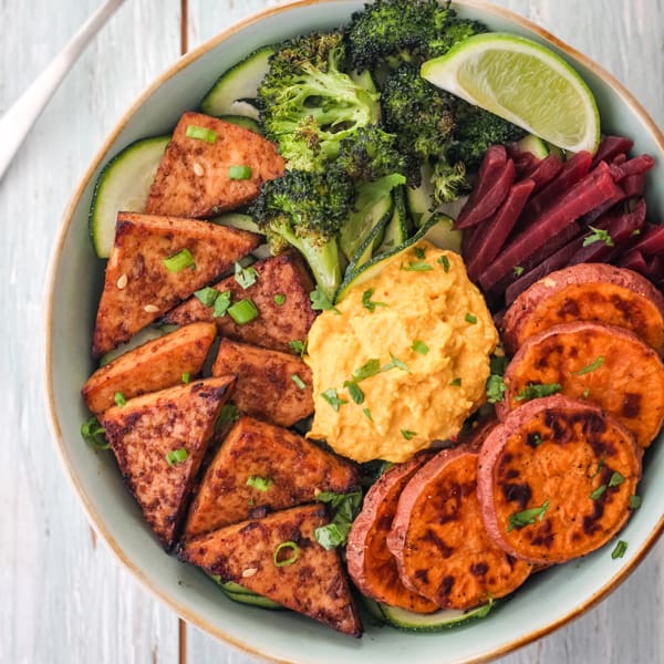 Broiled tofu in a bowl with zucchini spirals, sweet potato round, broccoli and hummus.