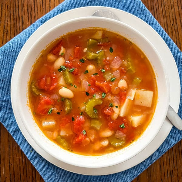 Bowl of vegetable soup on a plate with a spoon.