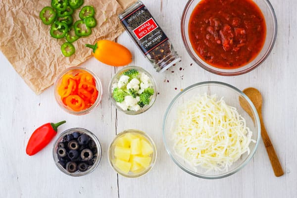 Bowls of marinara sauce, shredded cheese, and chopped vegetables.