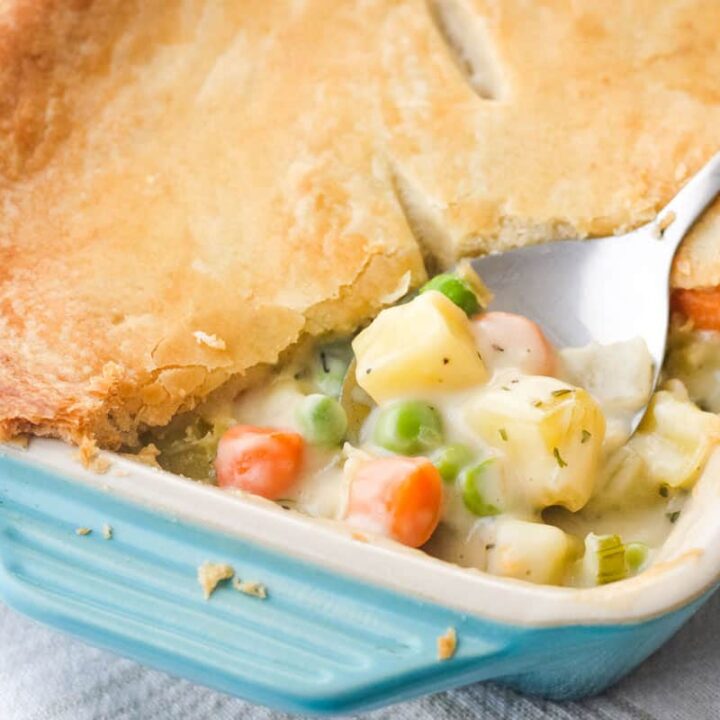 Closeup of spoon scooping creamy vegetable pot pie filling and crust from a small baking dish.