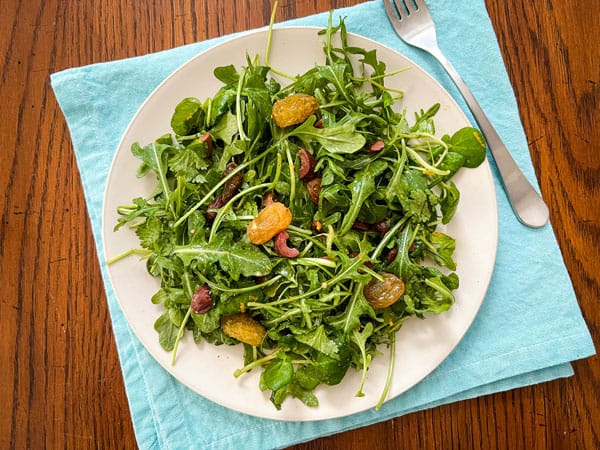 Overhead view of salad on a plate with a blue napkin and fork.