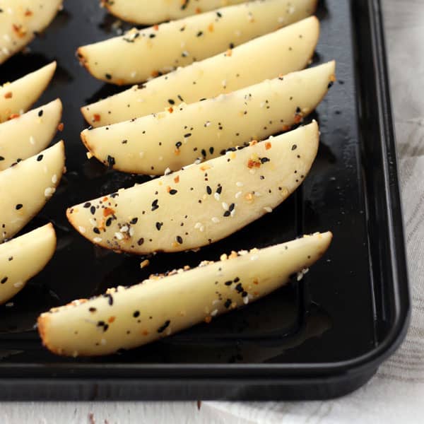 Seasoned wedges arranged skin-side-down on a roasting pan.