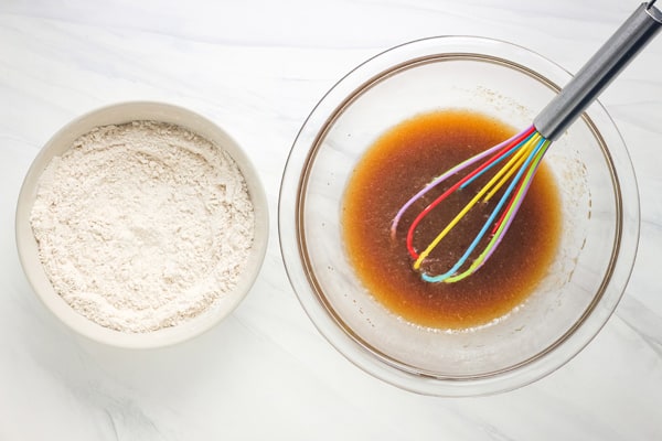 Bowls of dry ingredients and wet ingredients with a colorful whisk.