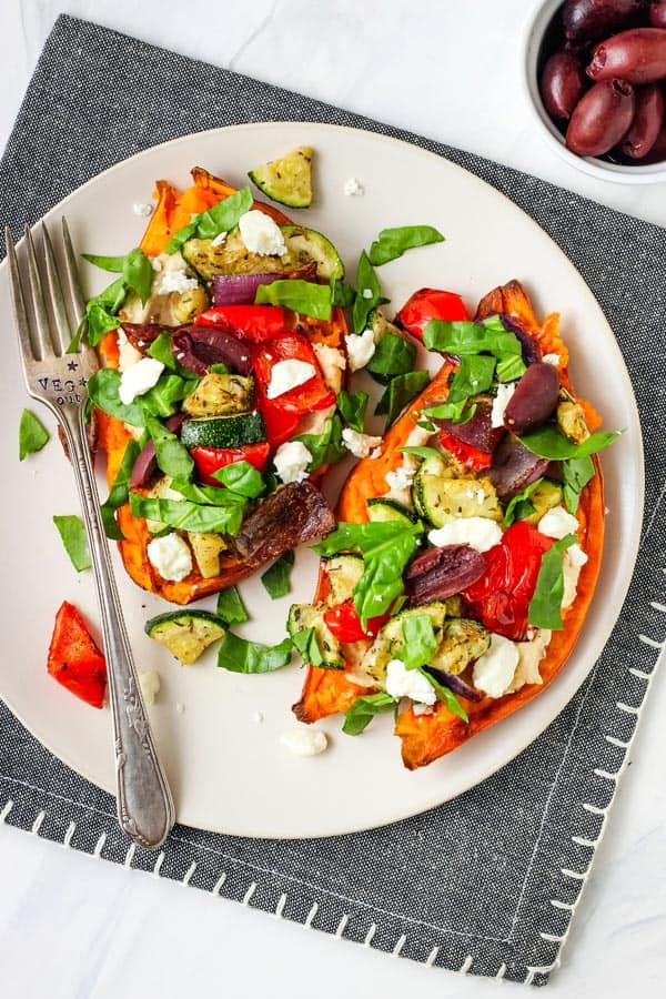 Two baked sweet potato halves with veggies, hummus, and feta cheese.